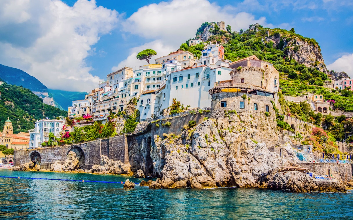 Amalfi Coast cliffside village with colorful buildings and lush greenery, viewed from the sea.
