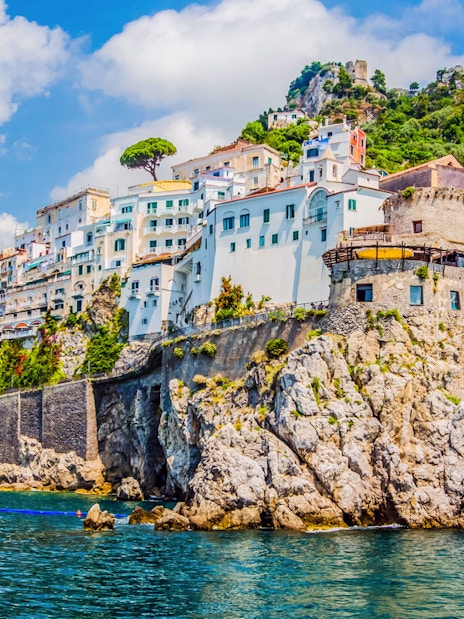 Amalfi Coast cliffside village with colorful buildings and lush greenery, viewed from the sea.