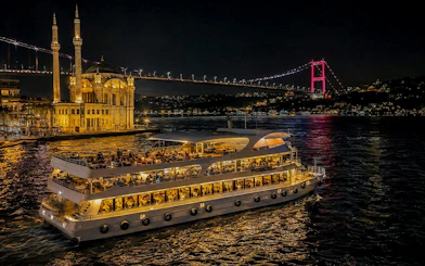Yacht cruise on Bosphorus at night with illuminated bridge and mosque, Istanbul.
