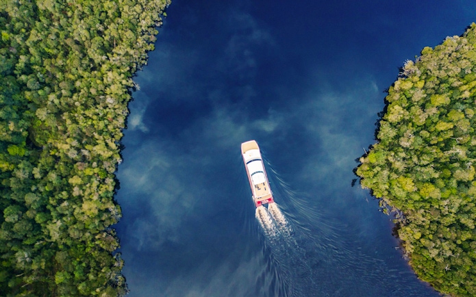 Cruise boat on Gordon River surrounded by lush forest, Strahan, Tasmania.