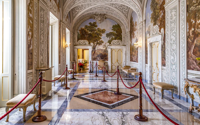 Ornate hallway inside Castle Gandolfo with frescoed walls and marble floors.
