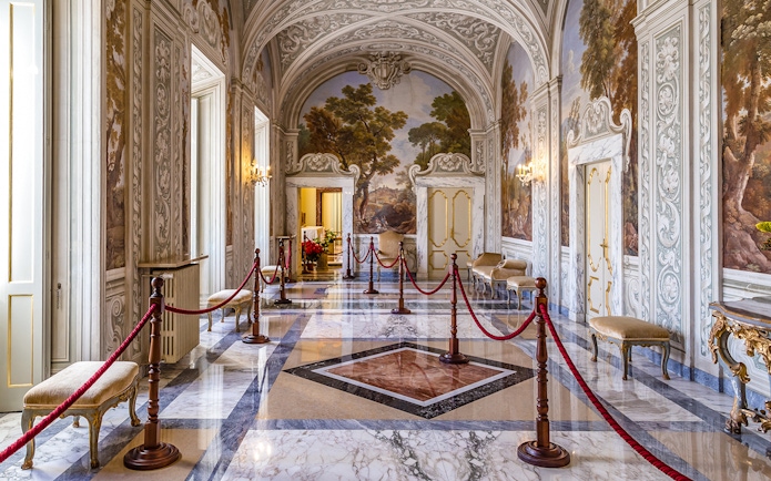 Ornate hallway inside Castle Gandolfo with frescoed walls and marble floors.