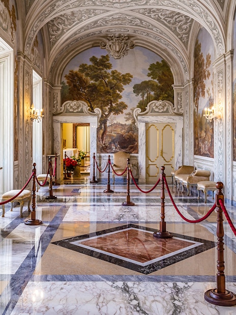 Ornate hallway inside Castle Gandolfo with frescoed walls and marble floors.