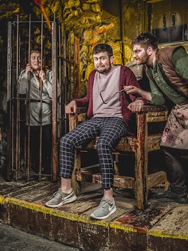 Man in stocks with actor holding tool at Edinburgh Dungeon.