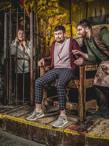 Man in stocks with actor holding tool at Edinburgh Dungeon.