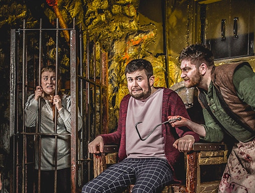Man in stocks with actor holding tool at Edinburgh Dungeon.