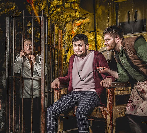 Man in stocks with actor holding tool at Edinburgh Dungeon.