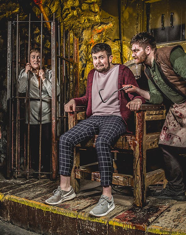 Man in stocks with actor holding tool at Edinburgh Dungeon.
