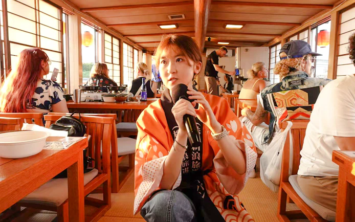 Tourist enjoying Yakatabune Hot Pot Cruise experience with microphone on traditional boat.