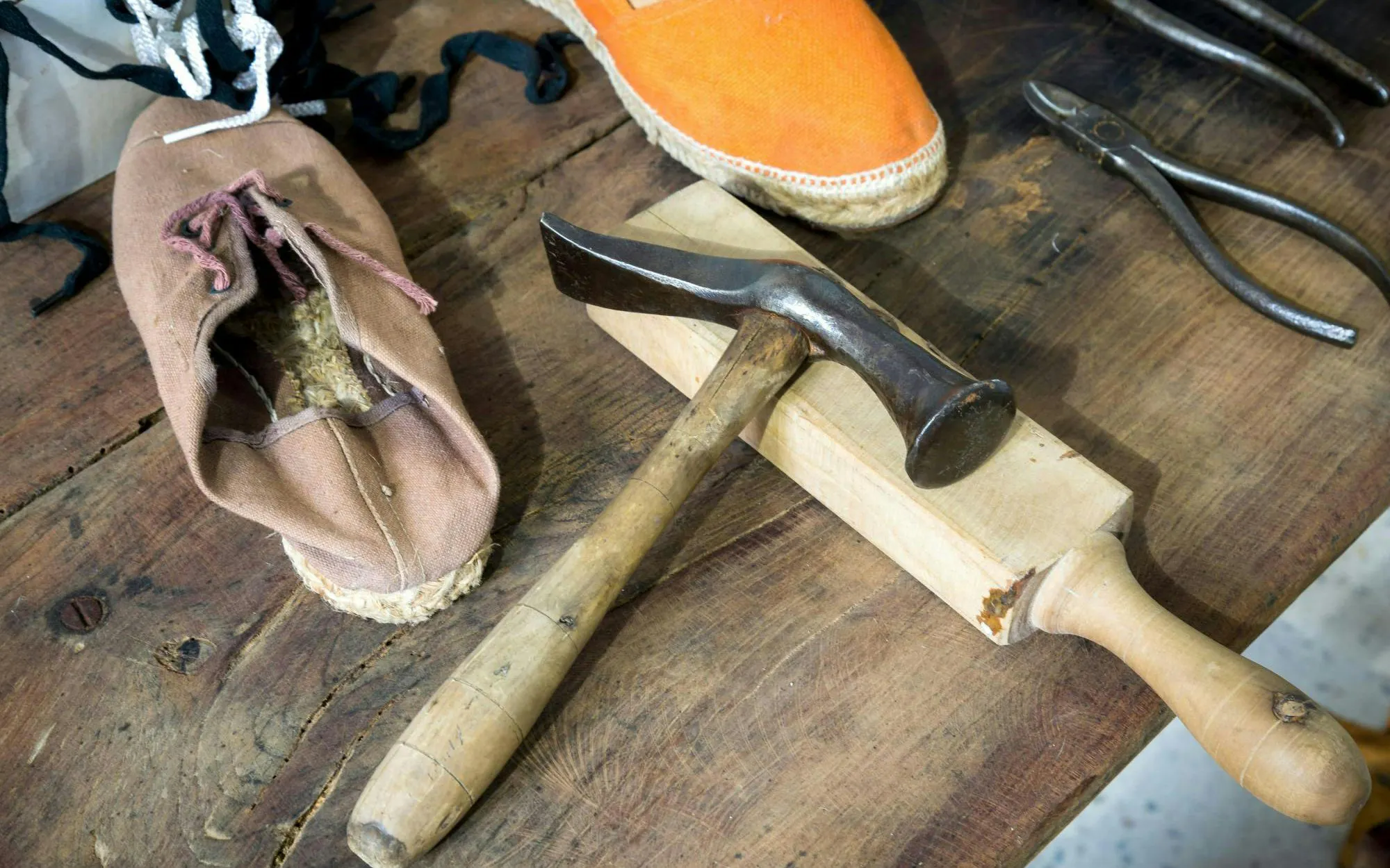 Traditional cobbler tools on a wooden table with a shoe and hammer.
