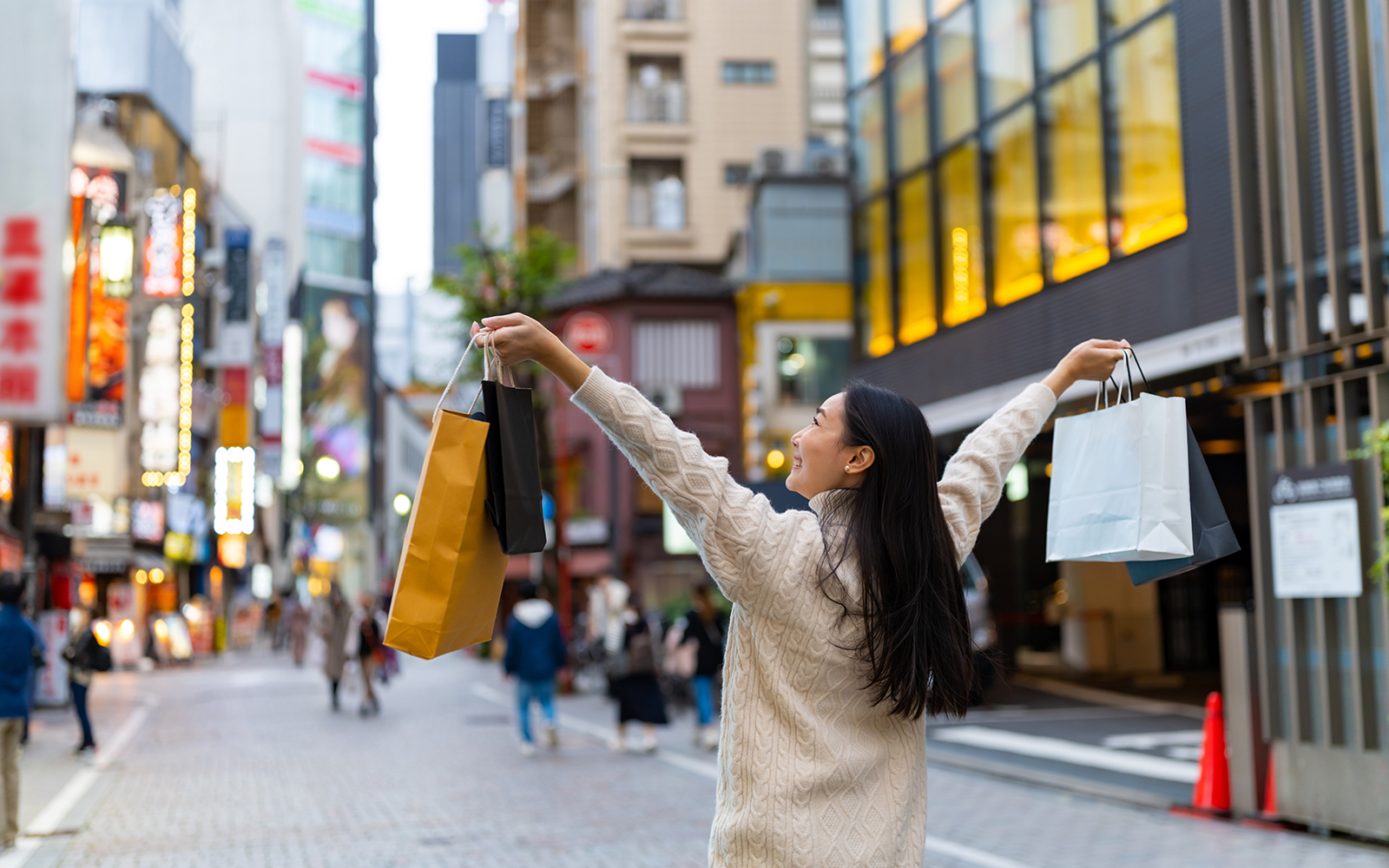Person shopping on a vibrant street in Tokyo, Japan, holding multiple shopping bags.