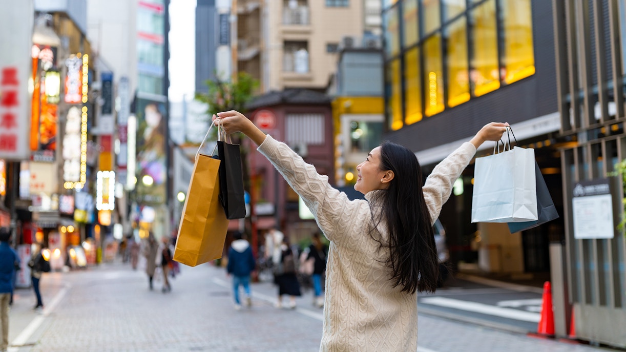Person shopping on a vibrant street in Tokyo, Japan, holding multiple shopping bags.