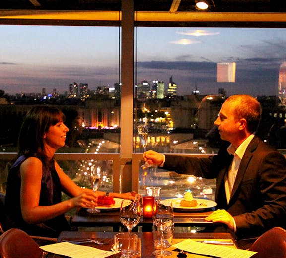 Dining couple with Eiffel Tower view in Paris restaurant.