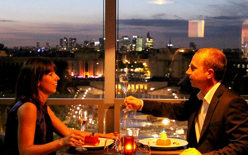 Dining couple with Eiffel Tower view in Paris restaurant.