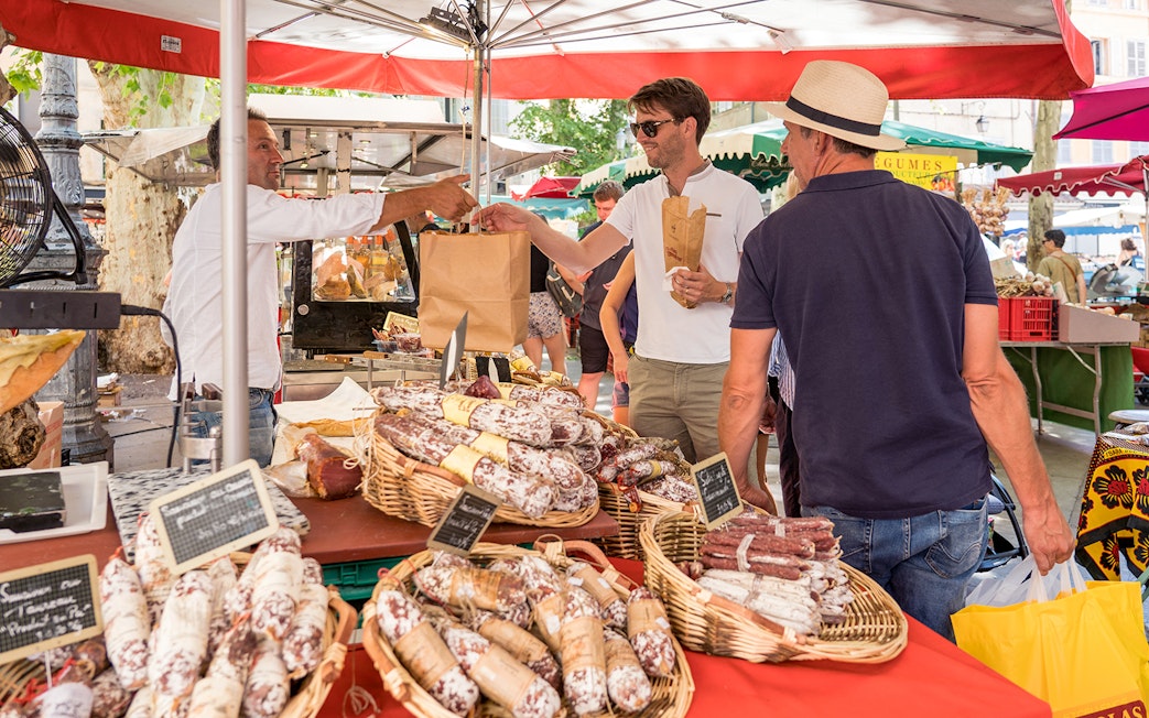 Market stall with people buying cured sausages during Lavender Full Day Tour in Provence.
