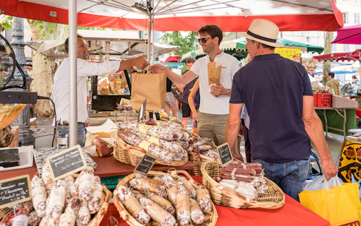 Market stall with people buying cured sausages during Lavender Full Day Tour in Provence.