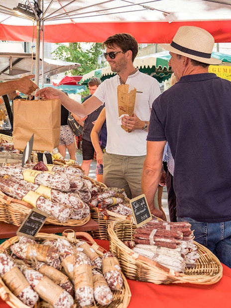 Market stall with people buying cured sausages during Lavender Full Day Tour in Provence.