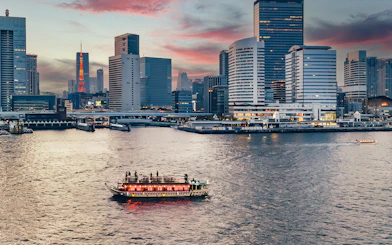 Yakatabune boat on Tokyo river at sunset with city skyline in background.