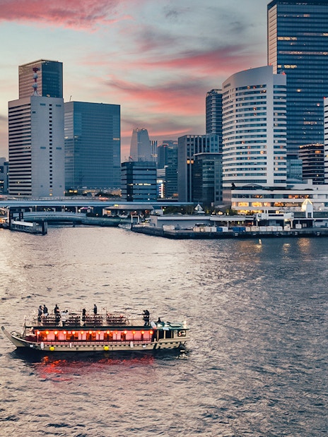 Yakatabune boat on Tokyo river at sunset with city skyline in background.