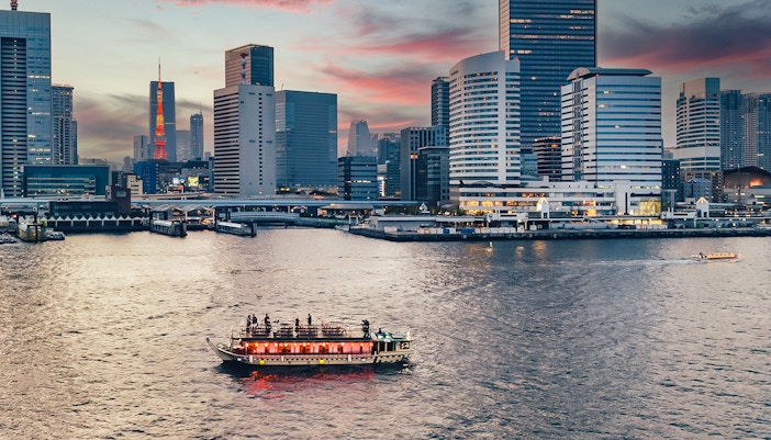 Yakatabune boat on Tokyo river at sunset with city skyline in background.