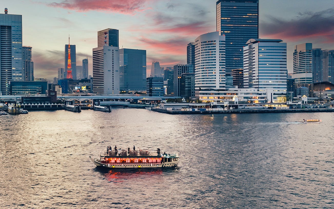 Yakatabune boat on Tokyo river at sunset with city skyline in background.
