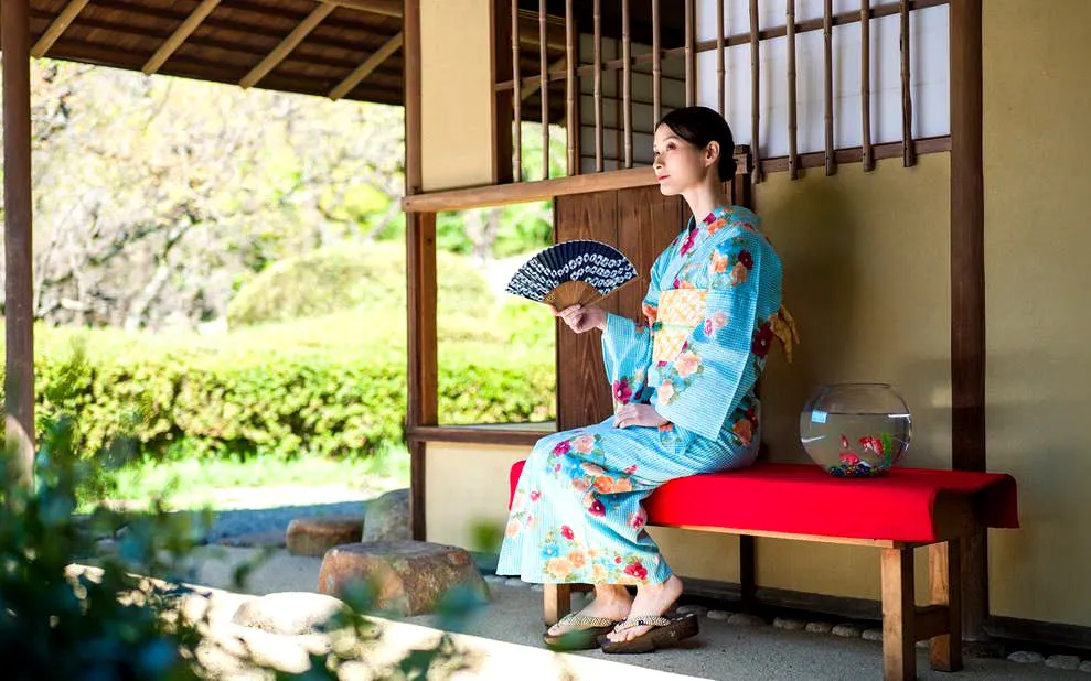 Kimono-clad person with fan seated in Shinjuku Gyoen National Garden, Tokyo.