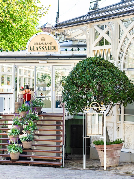 Glass restaurant entrance at Tivoli Gardens, Copenhagen with potted plants and decorative facade.