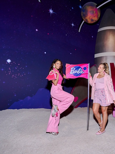 Guests holding a Barbie flag in front of a space-themed backdrop at Barbie, The Dream Experience.