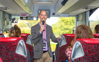 Tour guide speaking to passengers on a coach transfer.