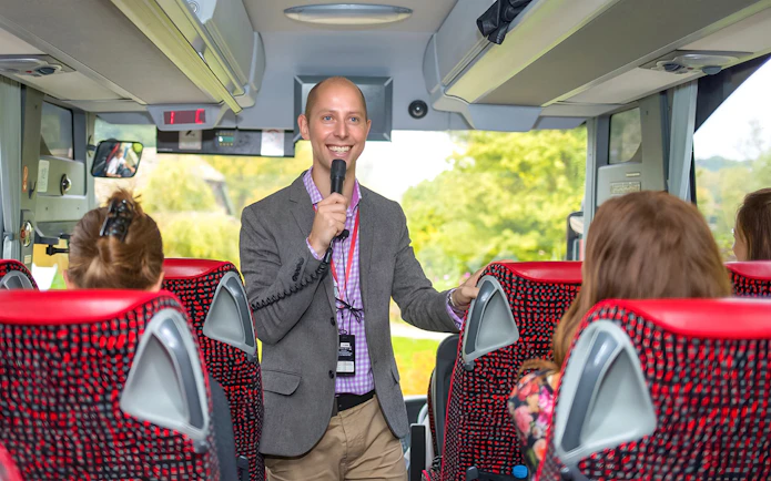 Tour guide speaking to passengers on a coach transfer.