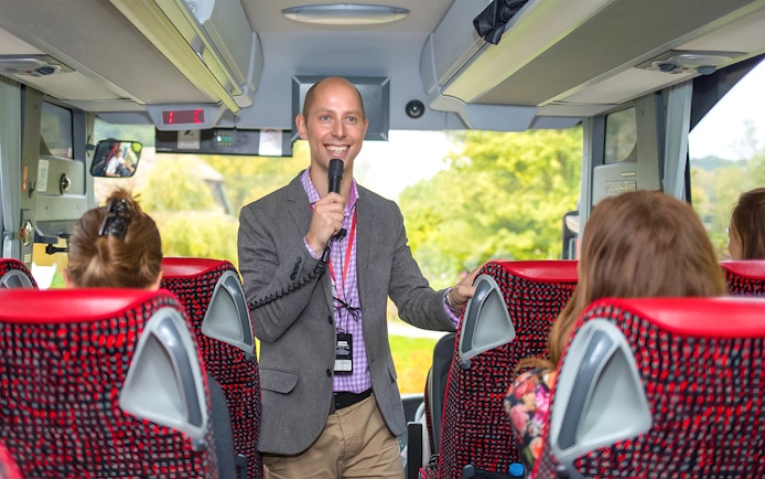 Tour guide speaking to passengers on a coach transfer.