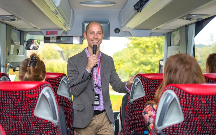 Tour guide speaking to passengers on a coach transfer.