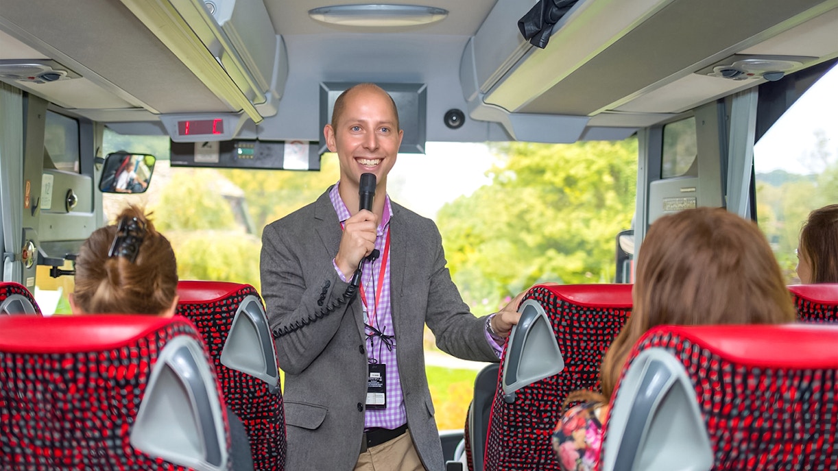 Tour guide speaking to passengers on a coach transfer.