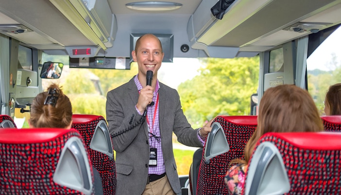 Tour guide speaking to passengers on a coach transfer.