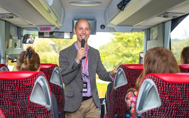 Tour guide speaking to passengers on a coach transfer.