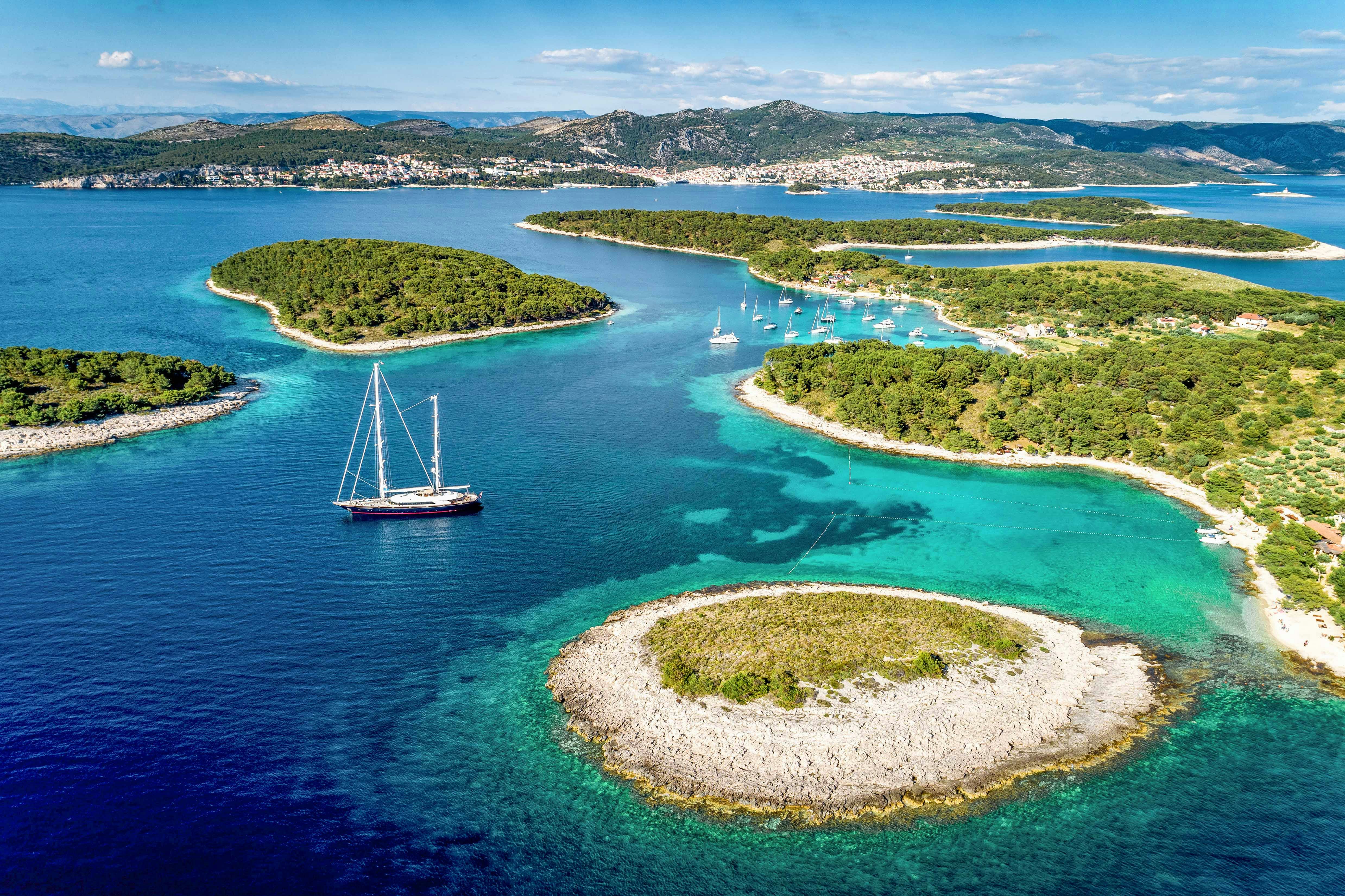 Sailboat navigating between lush Pakleni Islands, Croatia, with clear turquoise waters.
