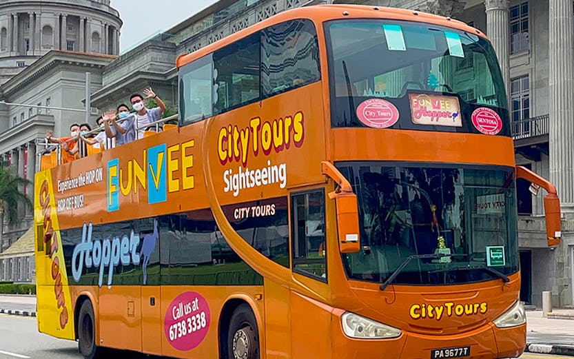 Open-top FunVee bus on a city tour in Singapore with passengers waving.