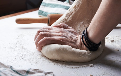 Hands kneading pizza dough during a cooking class.