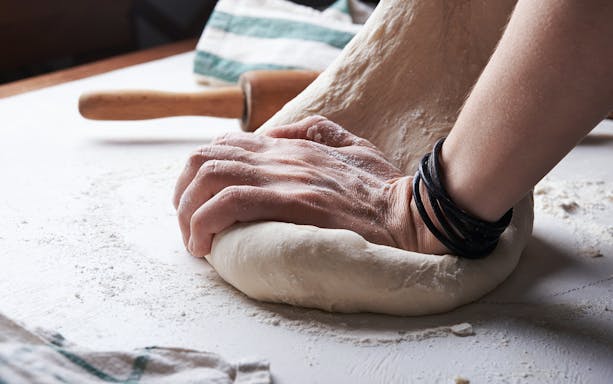 Hands kneading pizza dough during a cooking class.