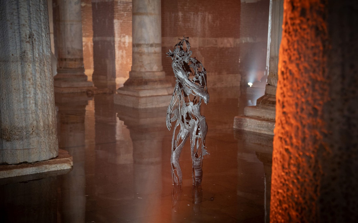 Sculpture in Basilica Cistern, Istanbul, surrounded by ancient columns and water reflections.