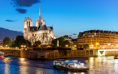 Seine River cruise boat passing Notre-Dame Cathedral at dusk in Paris.
