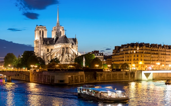 Seine River cruise boat passing Notre-Dame Cathedral at dusk in Paris.