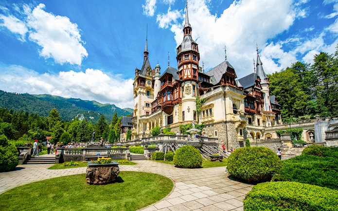 Peles Castle exterior with gardens and Carpathian Mountains in Sinaia, Romania.