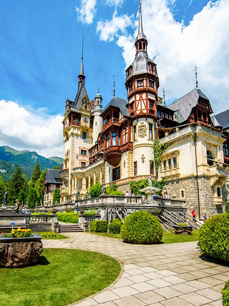 Peles Castle exterior with gardens and Carpathian Mountains in Sinaia, Romania.
