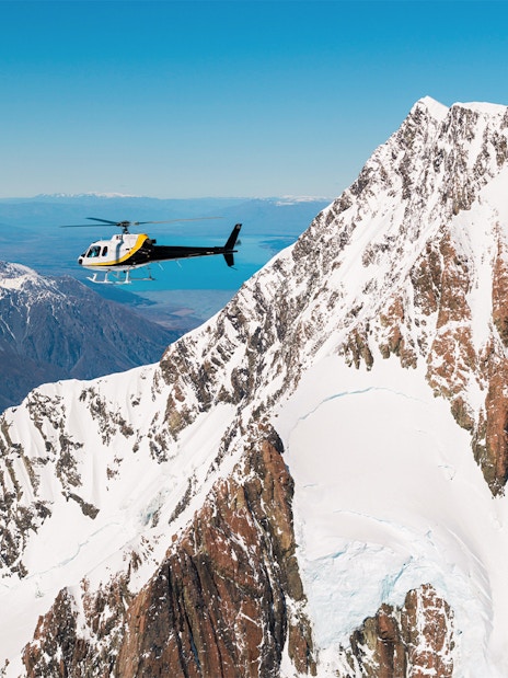 Helicopter flying near snow-covered Mt Cook with Lake Pukaki in the background.