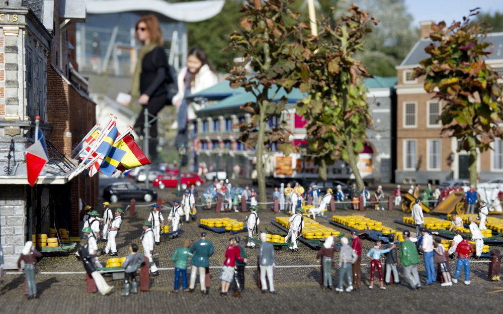 Miniature cheese market scene at Madurodam park, Netherlands, with tiny figures and flags.