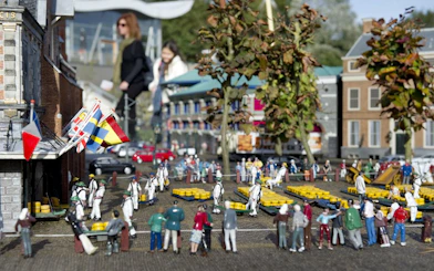 Miniature cheese market scene at Madurodam park, Netherlands, with tiny figures and flags.