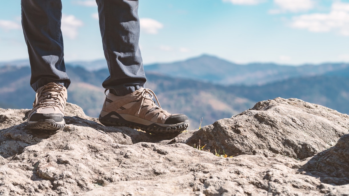 Trekking shoes on rocky terrain with mountain view in the background.