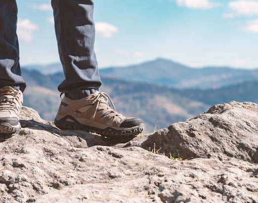 Trekking shoes on rocky terrain with mountain view in the background.