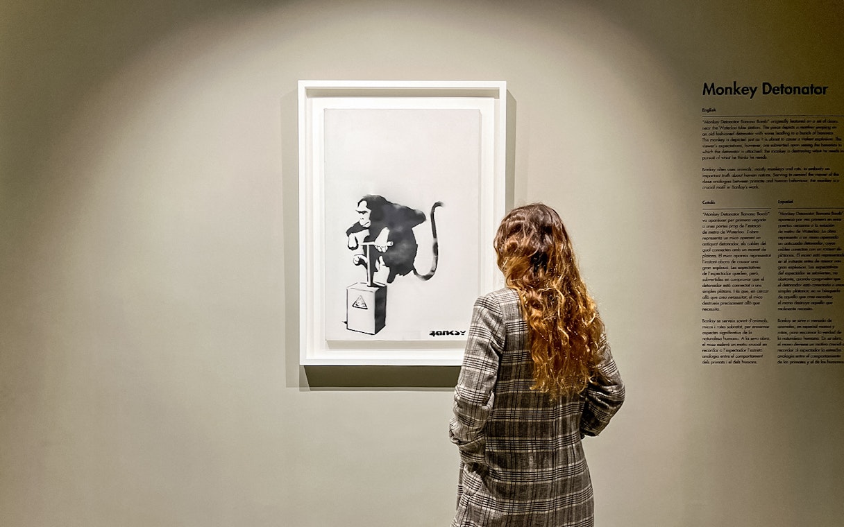Tourist viewing Banksy's "Monkey Detonator" artwork in a gallery.